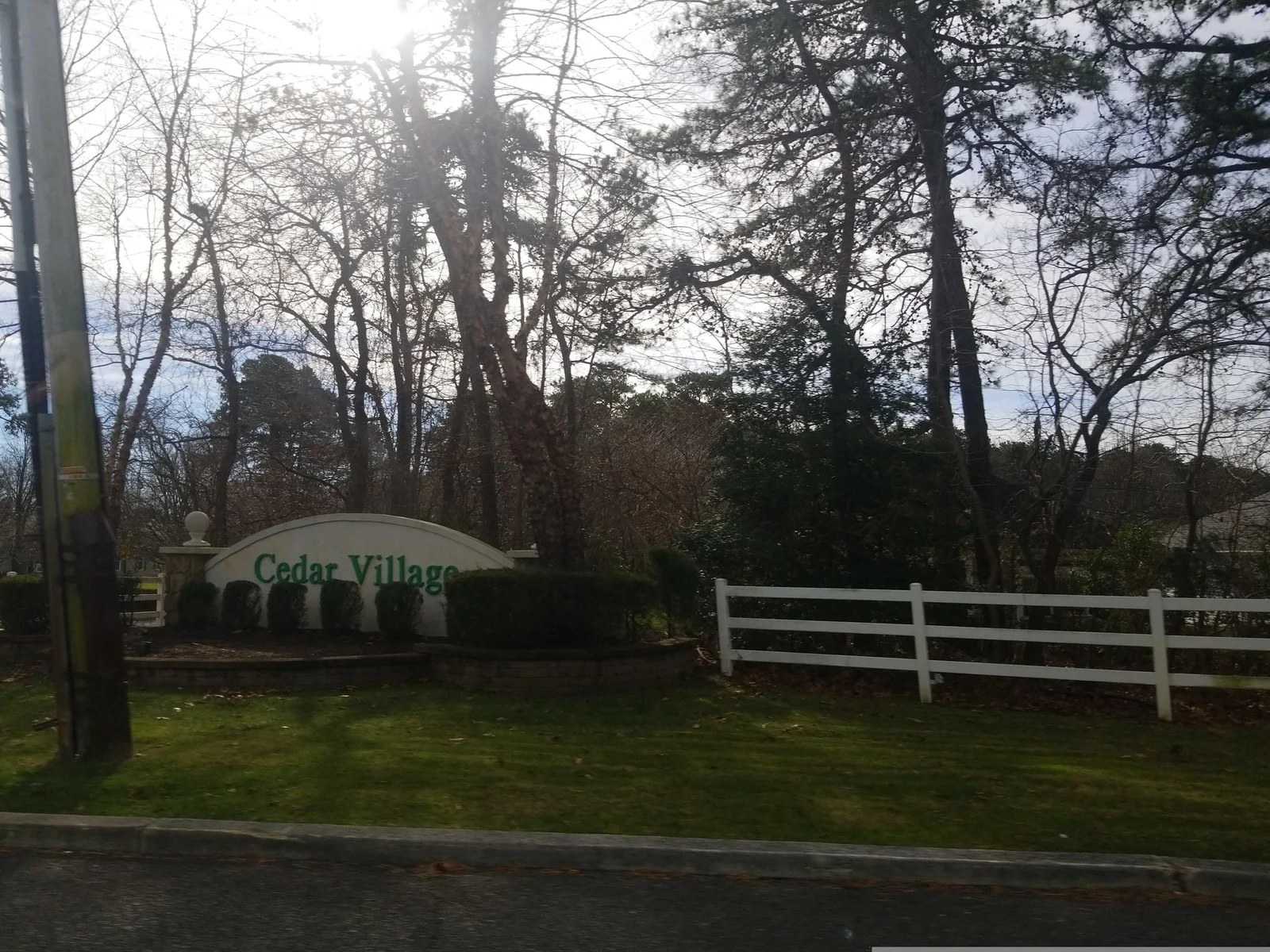Curved Cedar Village sign behind a lawn and white rail fence
