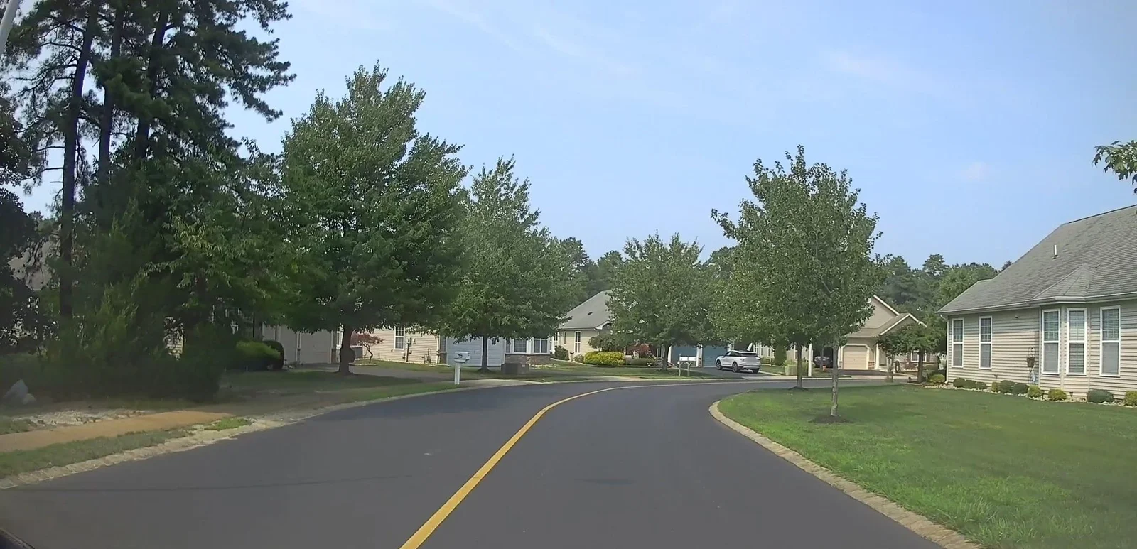 Street with a yellow center line, lawns and homes among trees