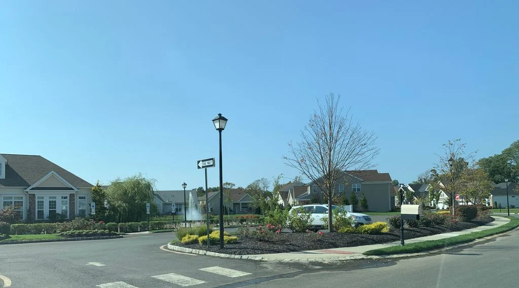 Landscaped traffic circle with lamp posts and plantings, clubhouse and homes in the background