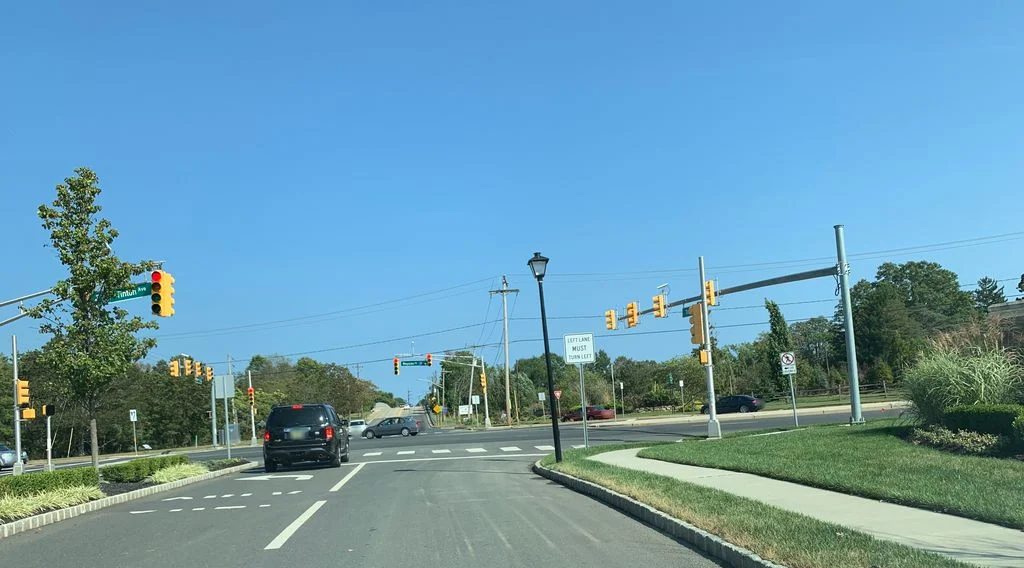 Divided entrance road with lamp posts and landscaped islands leading to a traffic light