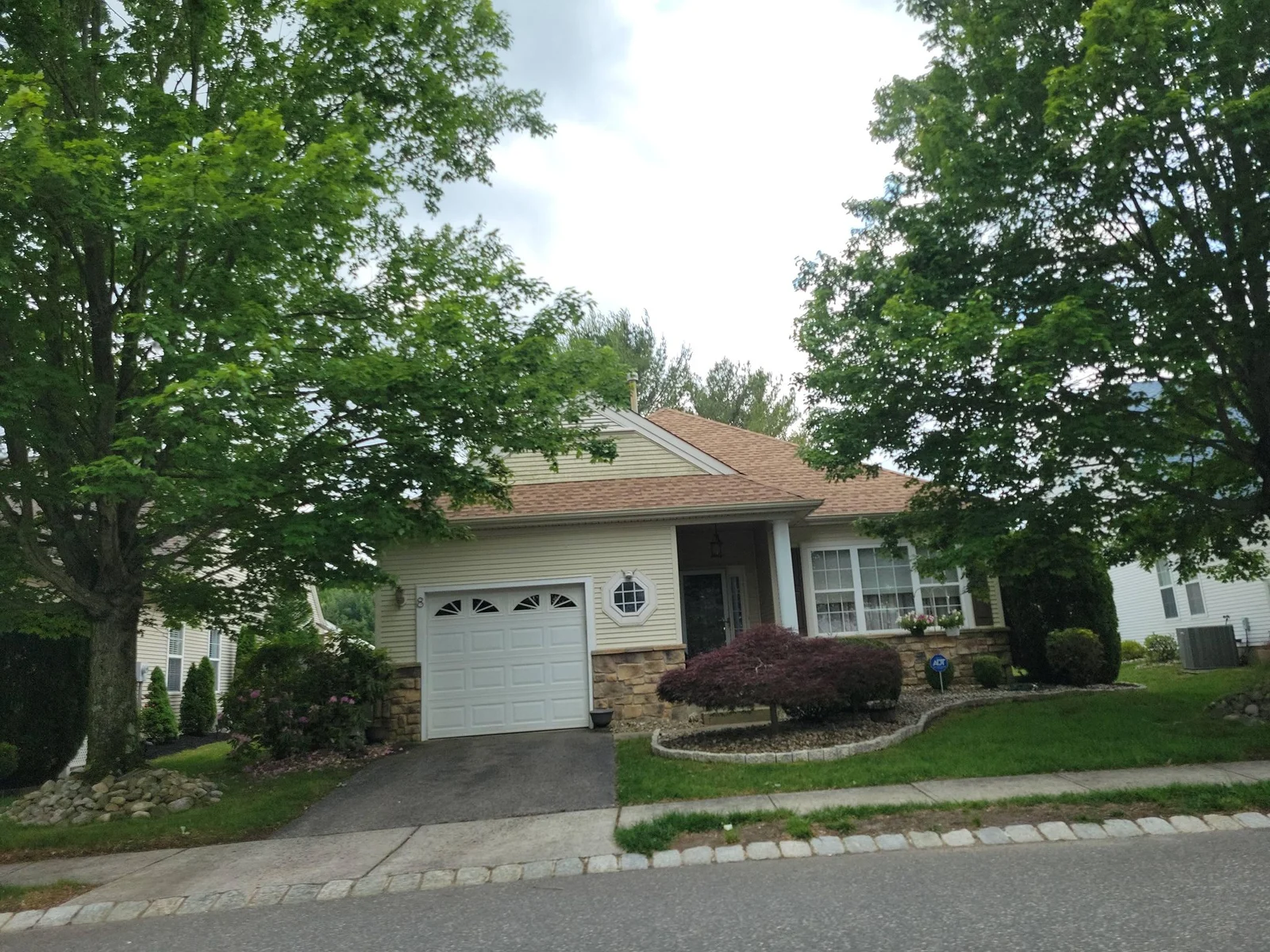 Single-story home with stone trim and a white garage door under trees