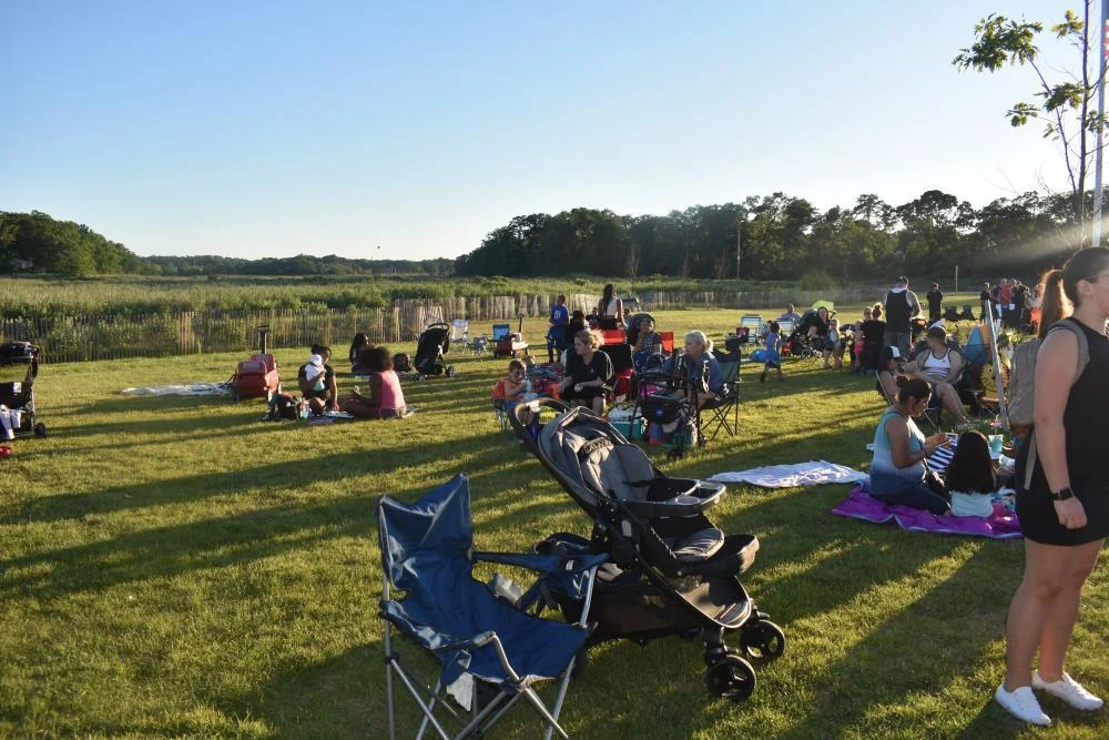 People on blankets and lawn chairs across a grassy field at golden hour, waiting for the township fireworks