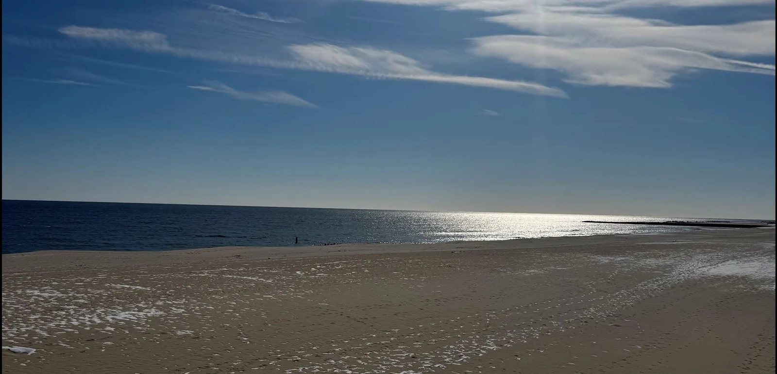 The wide, empty Allenhurst beach in December with sun glinting on the ocean