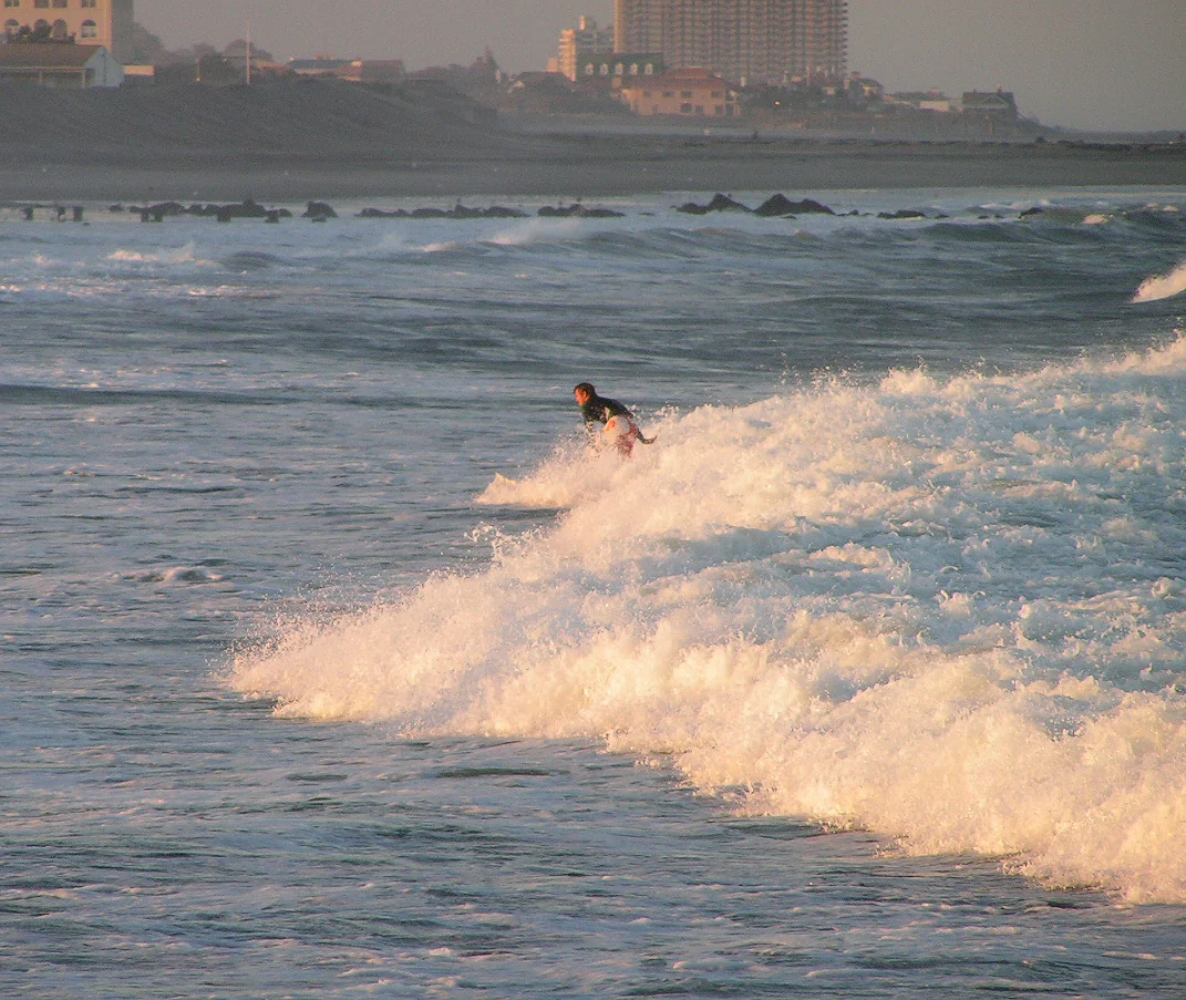 A surfer riding a breaking wave off Allenhurst in golden light