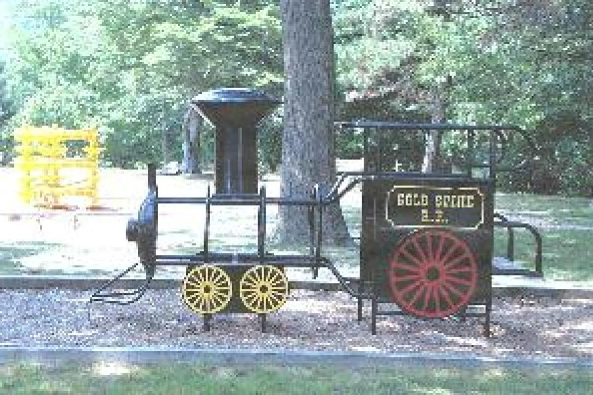 A black and red play train marked Gold Coast R.R. in a shady borough playground