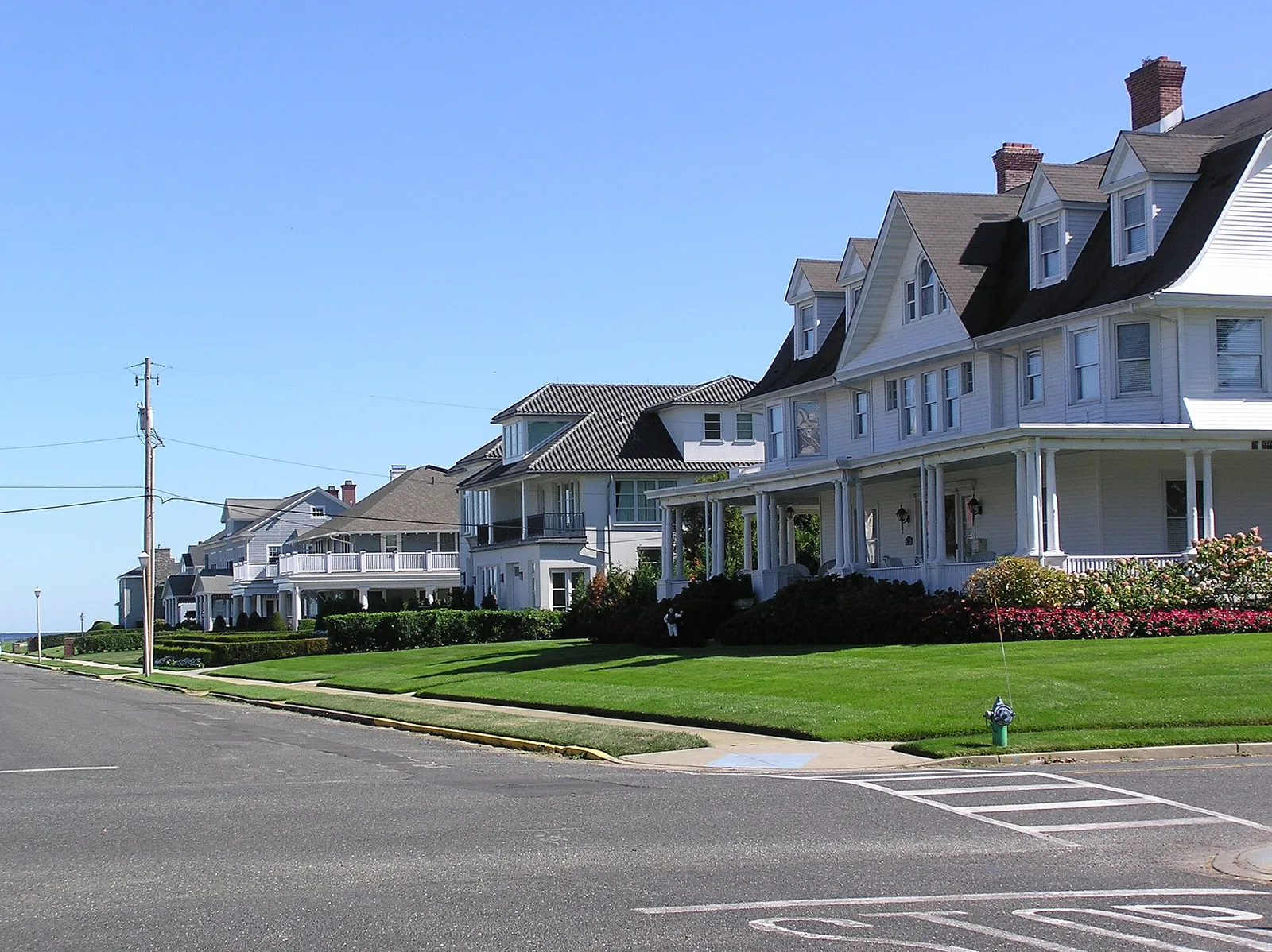 Large white shingle and clapboard homes with wide porches and green lawns on a corner in the Allenhurst Residential Historic District