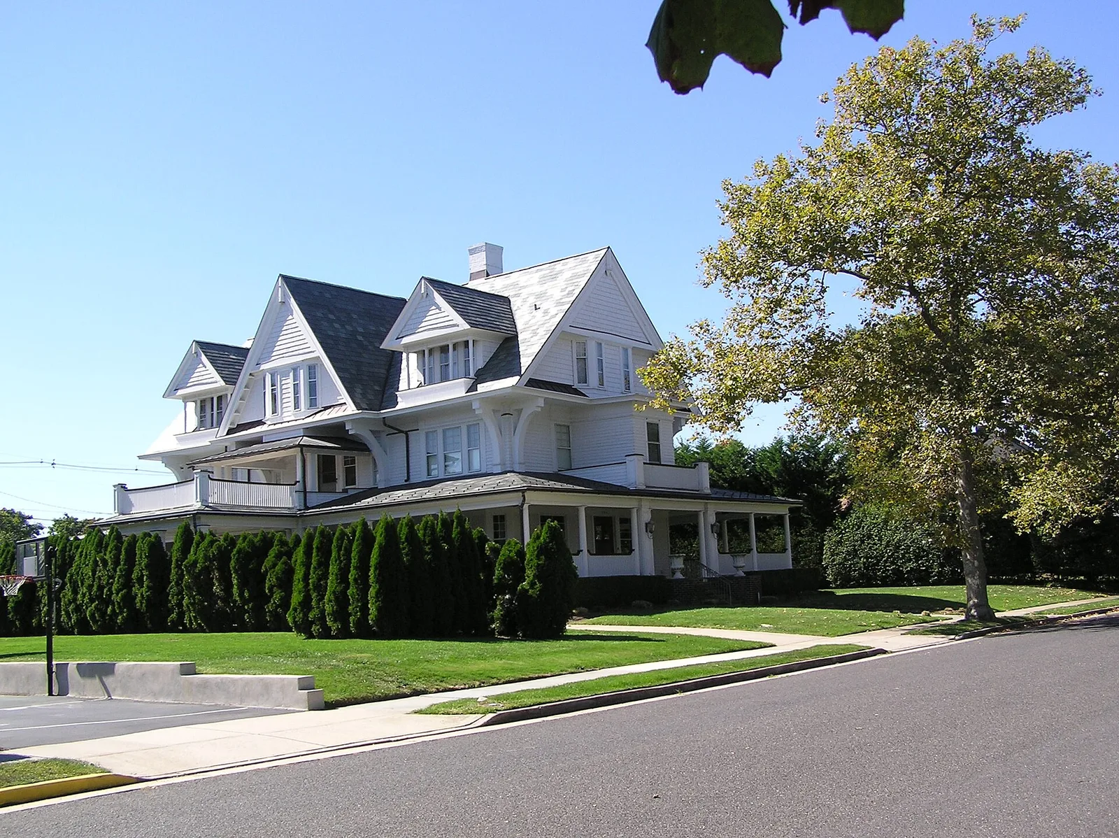A gabled historic home with a wraparound porch behind a hedge in Allenhurst