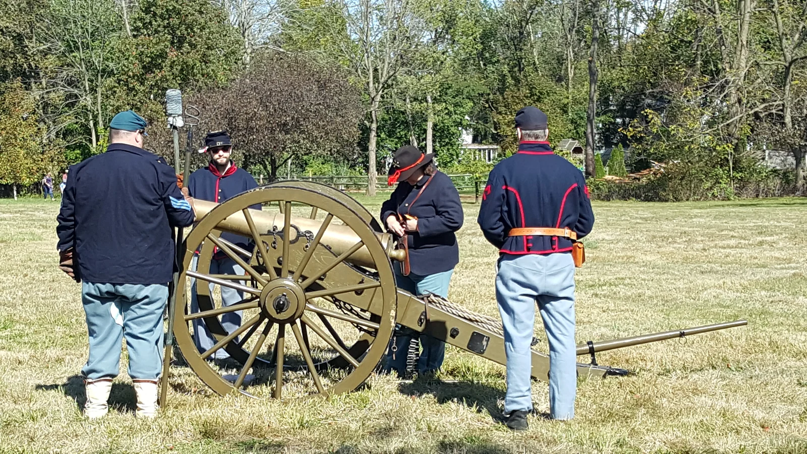 Civil War reenactors in blue uniforms gathered around a cannon on a grassy field at the Fall Festival