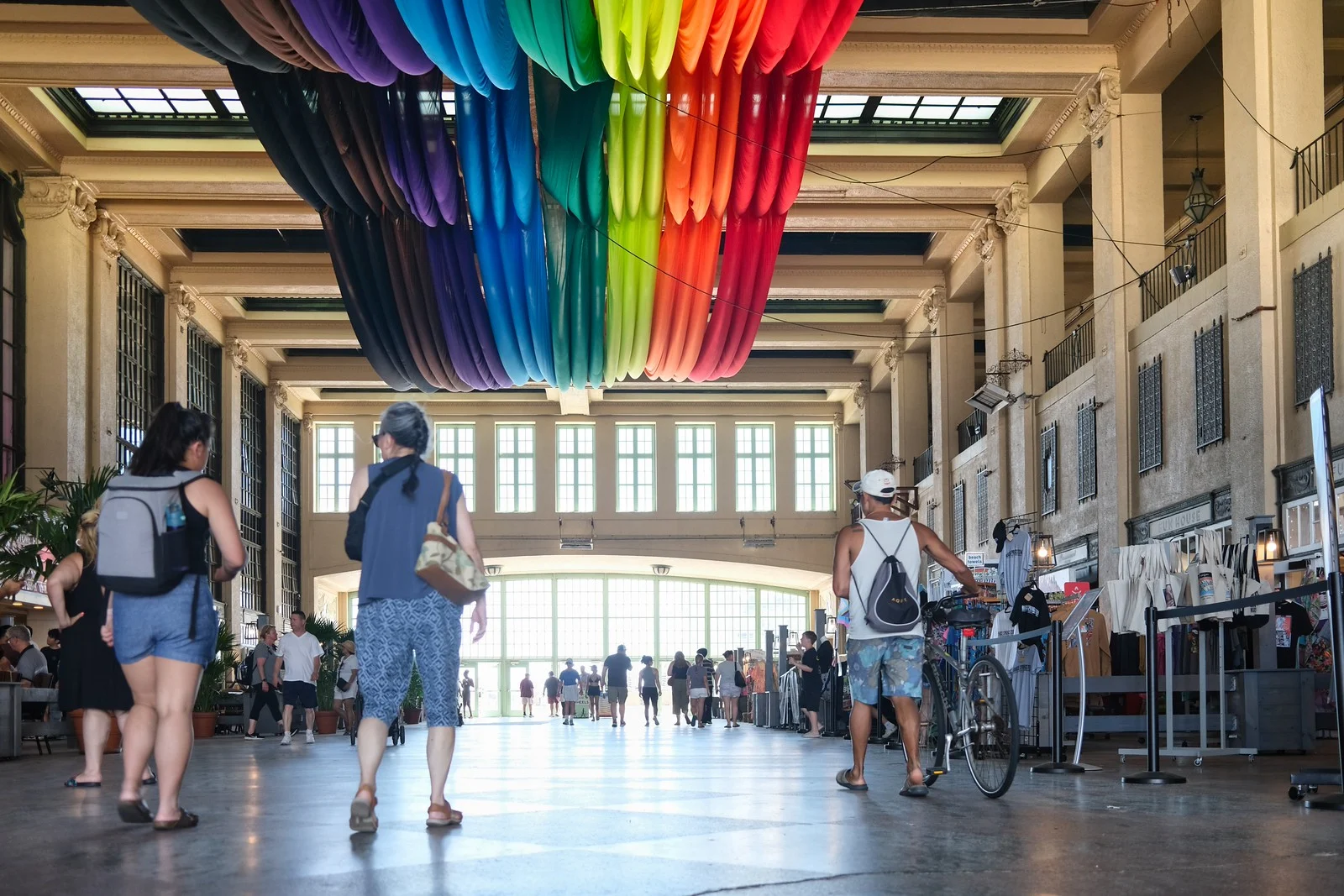 Visitors walking through the Grand Arcade inside Convention Hall under a ceiling of rainbow-colored fabric
