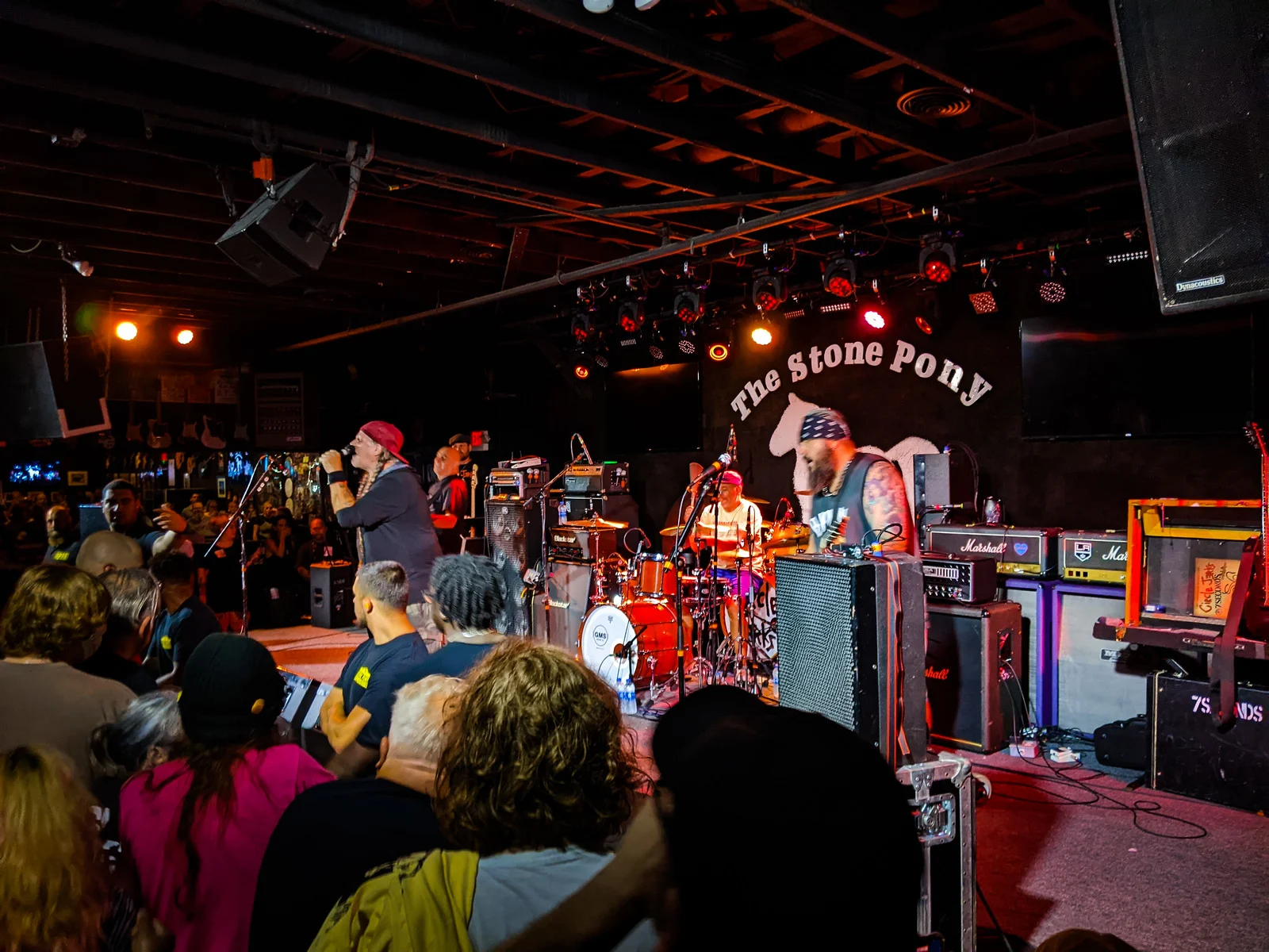 A punk band playing under colored stage lights at The Stone Pony, the club's horse logo on the wall behind a packed crowd