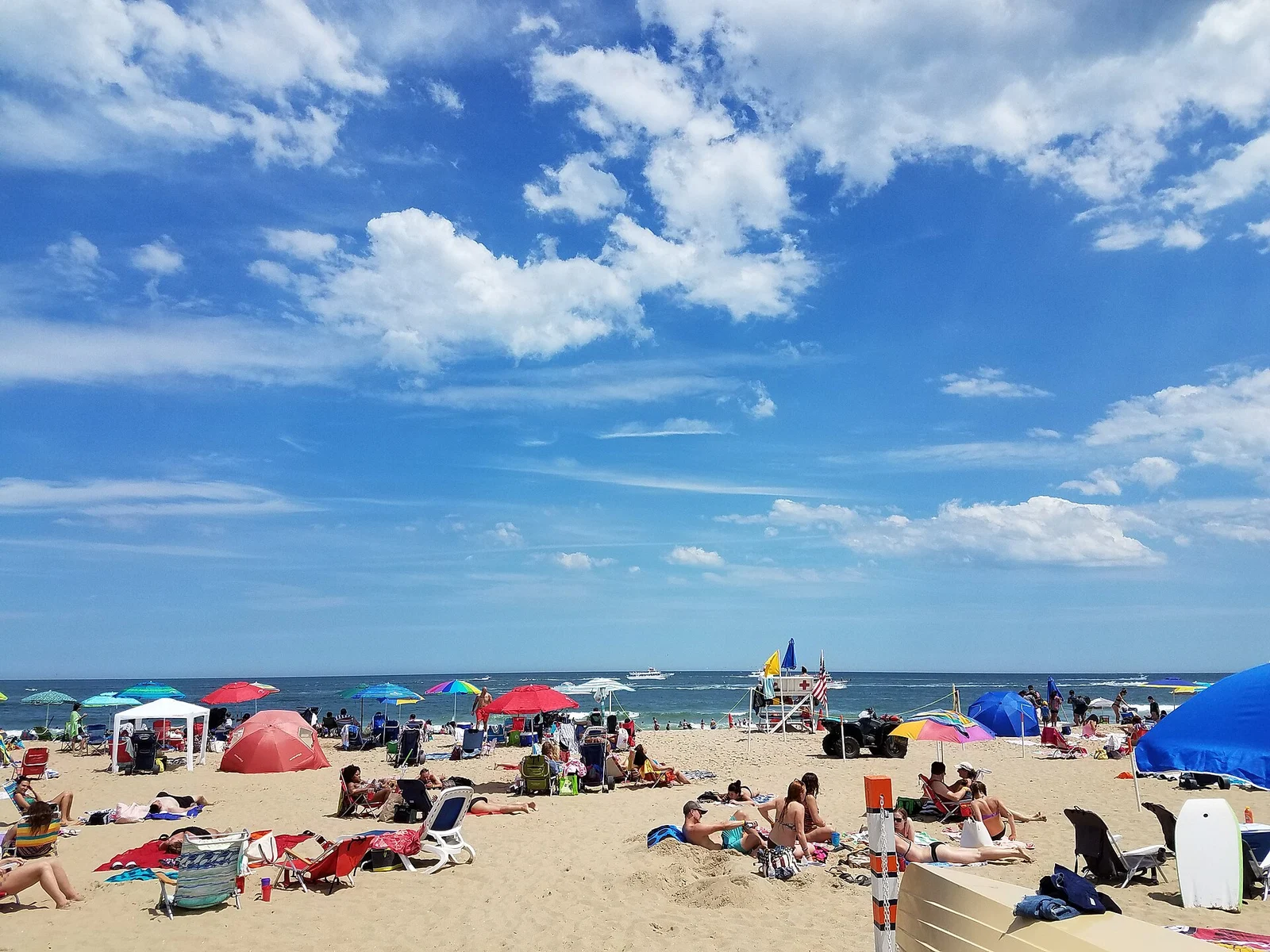 A busy summer beach with colorful umbrellas and beach towels on the sand below a bright blue sky