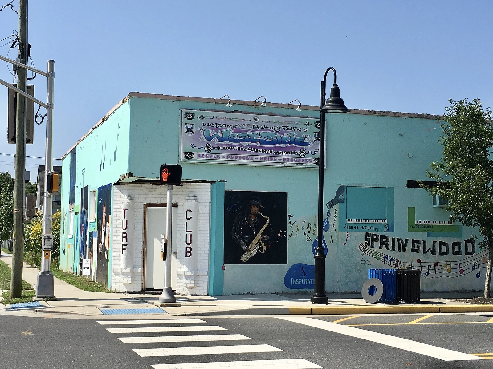 The pale blue Turf Club music venue on a street corner, with a painted saxophone player and a Springwood mural on its wall