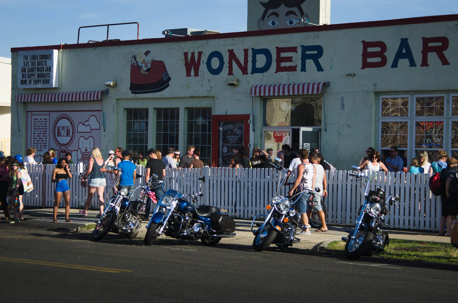 The white Wonder Bar with its red lettering and Tillie face, motorcycles parked out front and people along the fence