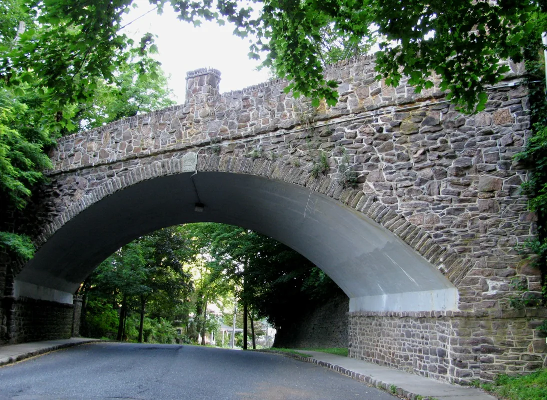 A stone arch bridge crossing over Grand Avenue under a canopy of green trees