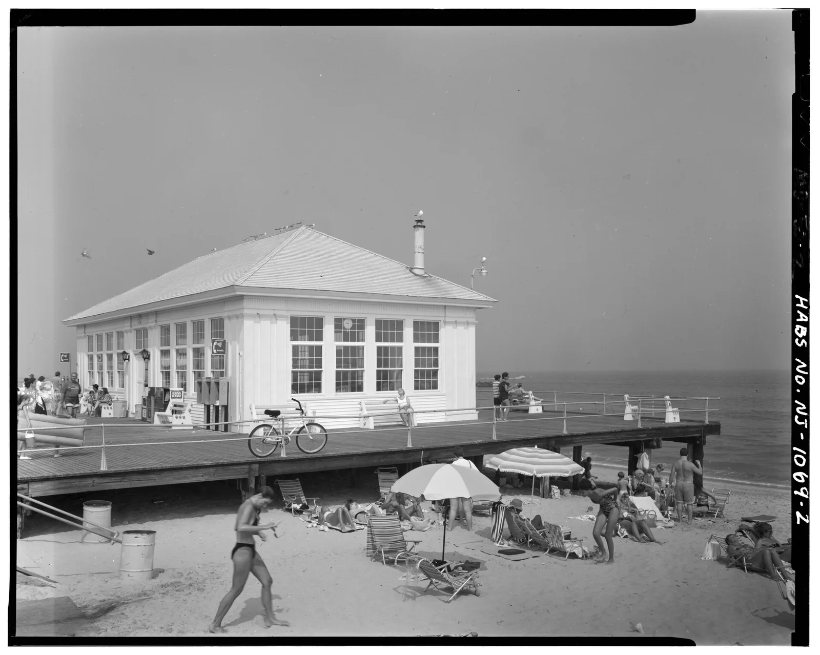 Historic black and white photo of a boardwalk pavilion in Avon-by-the-Sea with beachgoers on the sand below