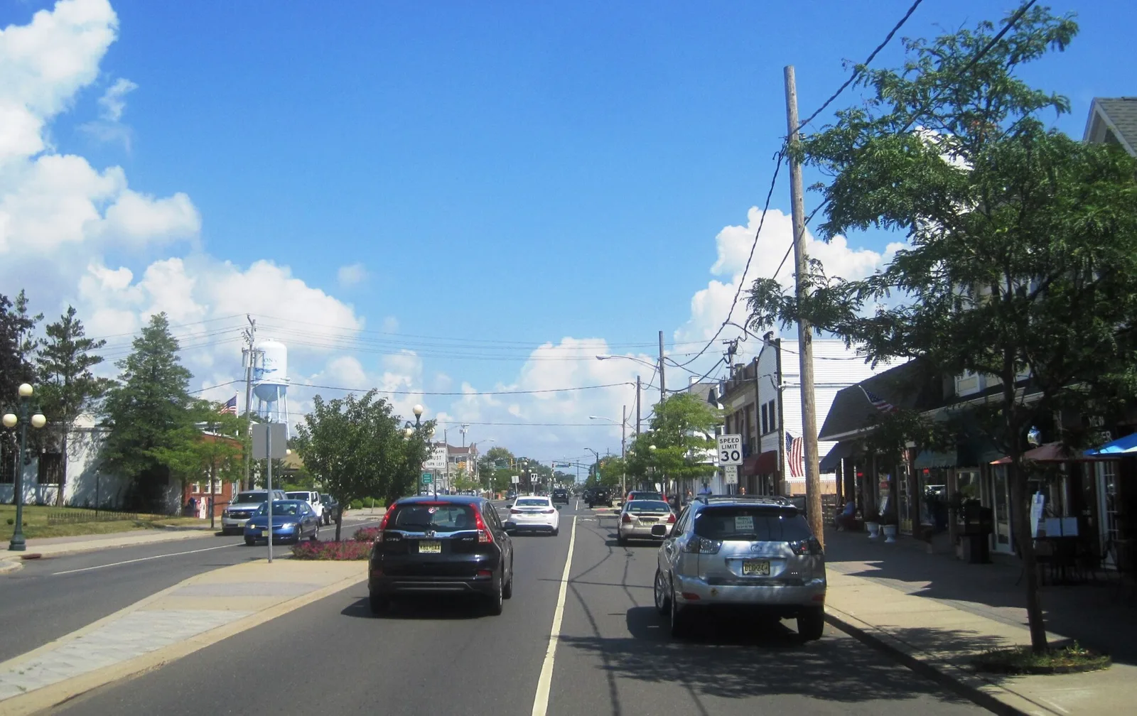 Main Street in Avon-by-the-Sea lined with shops, trees and parked cars on a sunny day