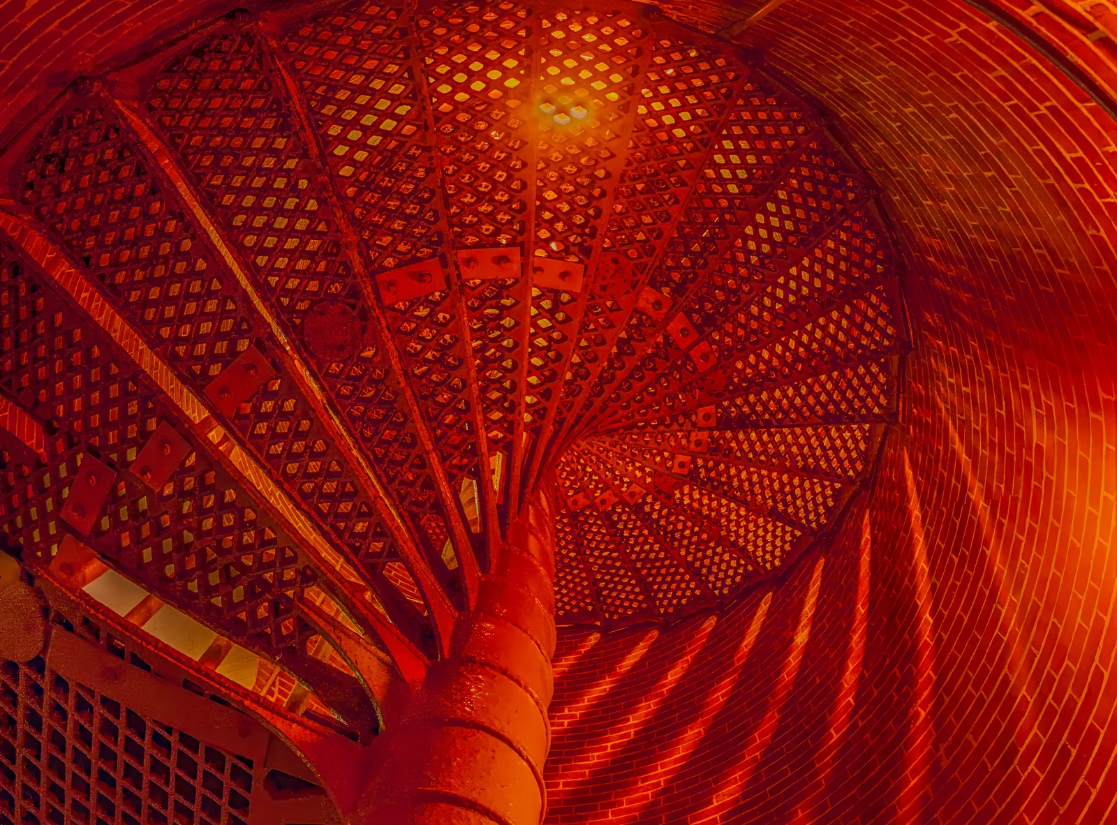Looking up the spiral iron staircase inside Barnegat Lighthouse, glowing red and orange against the brick walls