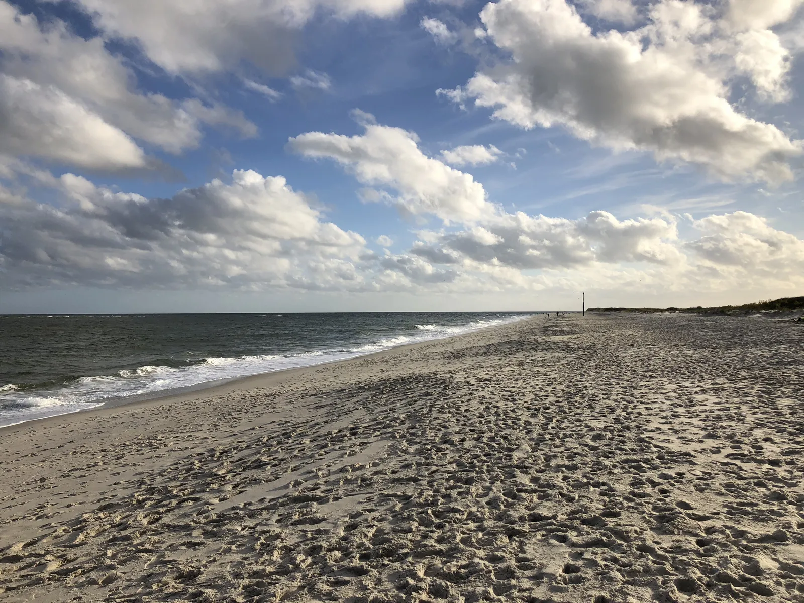 A wide sandy beach with gentle surf stretching into the distance under big white clouds