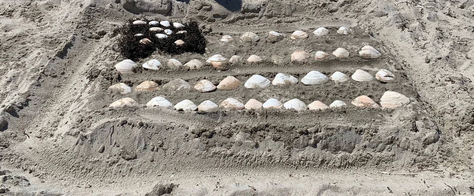 An American flag built from clam shells and seaweed in the sand at the borough sand sculpting contest