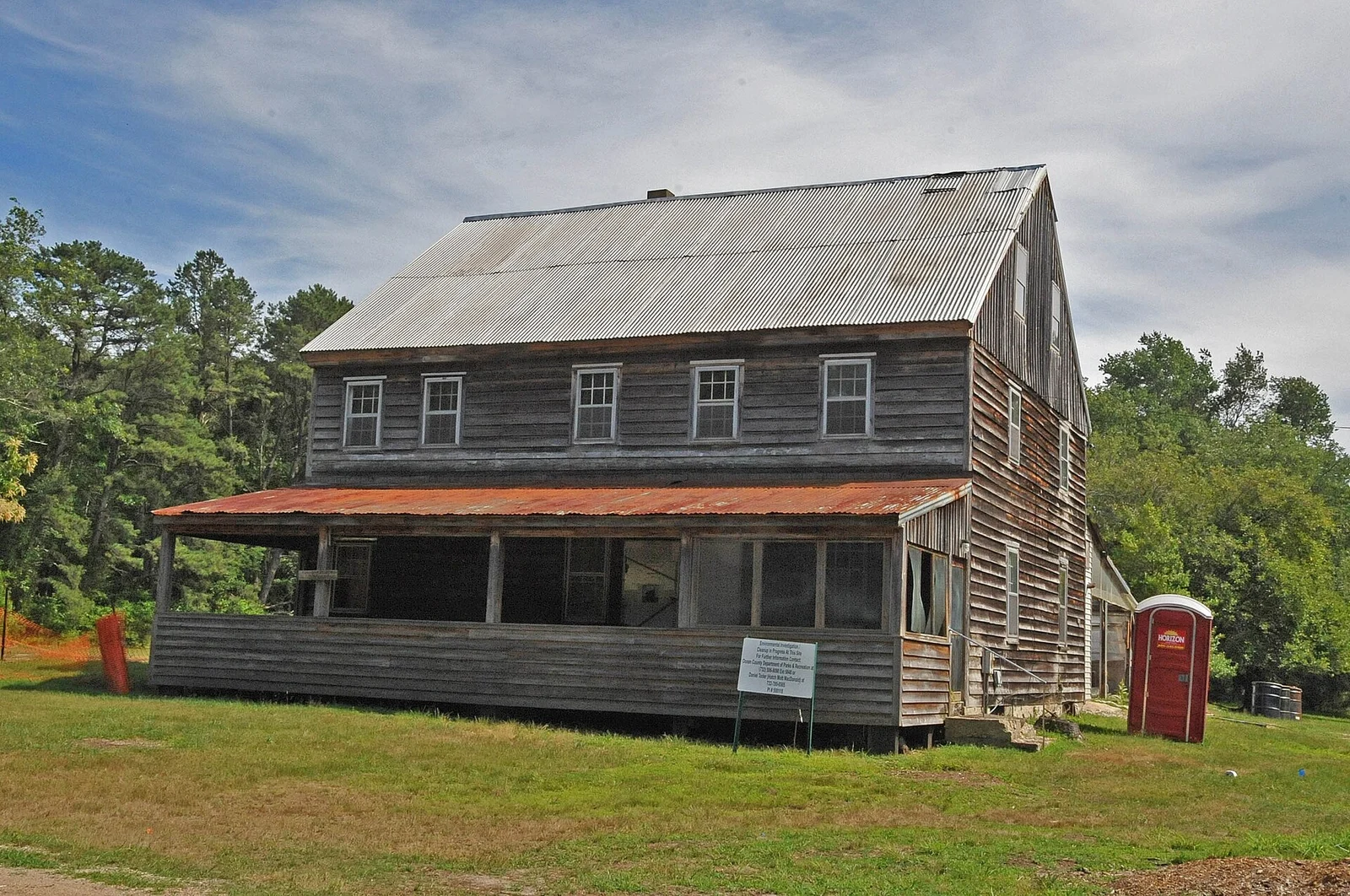The weathered two-story Cedar Bridge Tavern with its long front porch, set on a lawn at the edge of the pine forest
