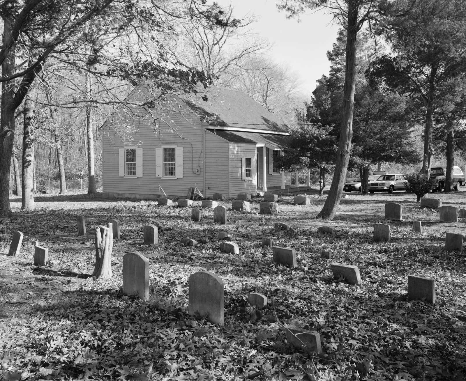 Black-and-white view of the small Quaker Meeting House behind rows of old gravestones under tall trees