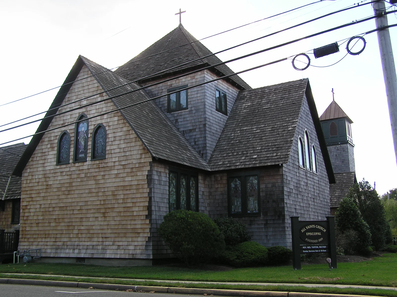 All Saints Episcopal Church, a shingled church with steep gables and a small bell tower, on a green lawn