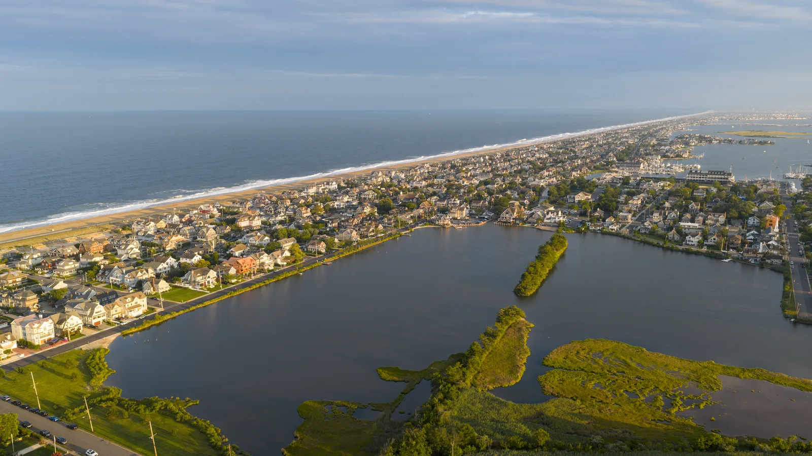 Bay Head from the air at dusk, rows of homes between a lake and marsh in front and the ocean beach beyond