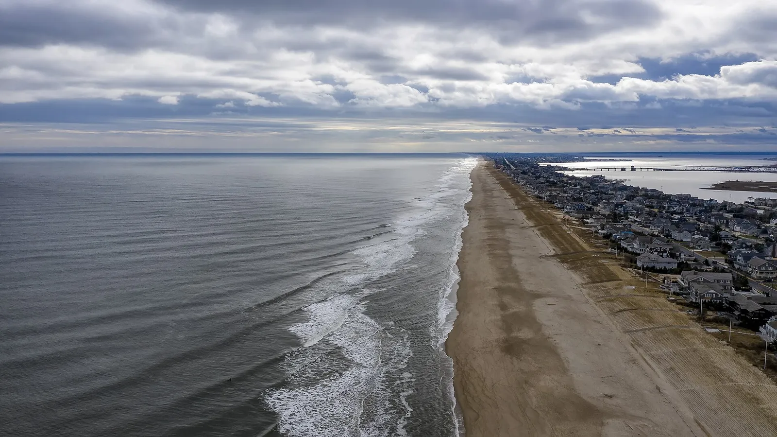 Aerial view of a long sandy beach with breaking waves and a row of shore homes