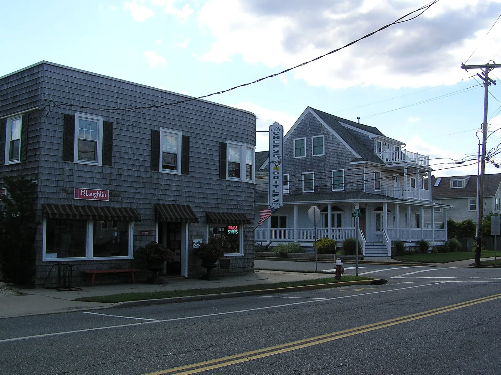 Gray cedar-shingled shop buildings on a street corner under a partly cloudy sky