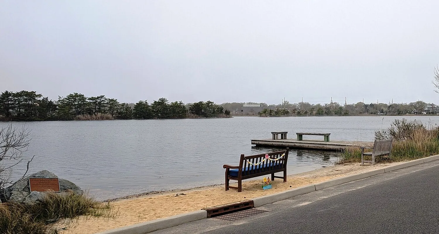 A calm lake with a small dock and a bench on a sandy shore