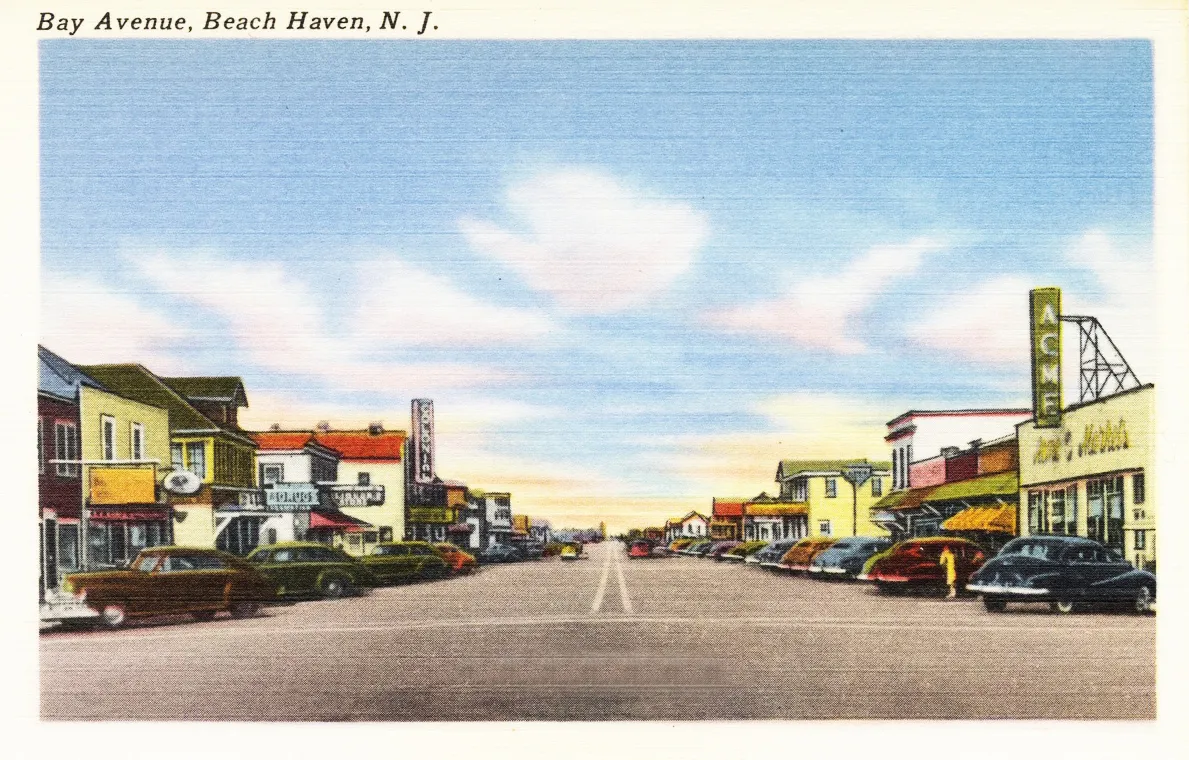 Vintage postcard of a wide main street lined with shops, signs and parked 1940s cars