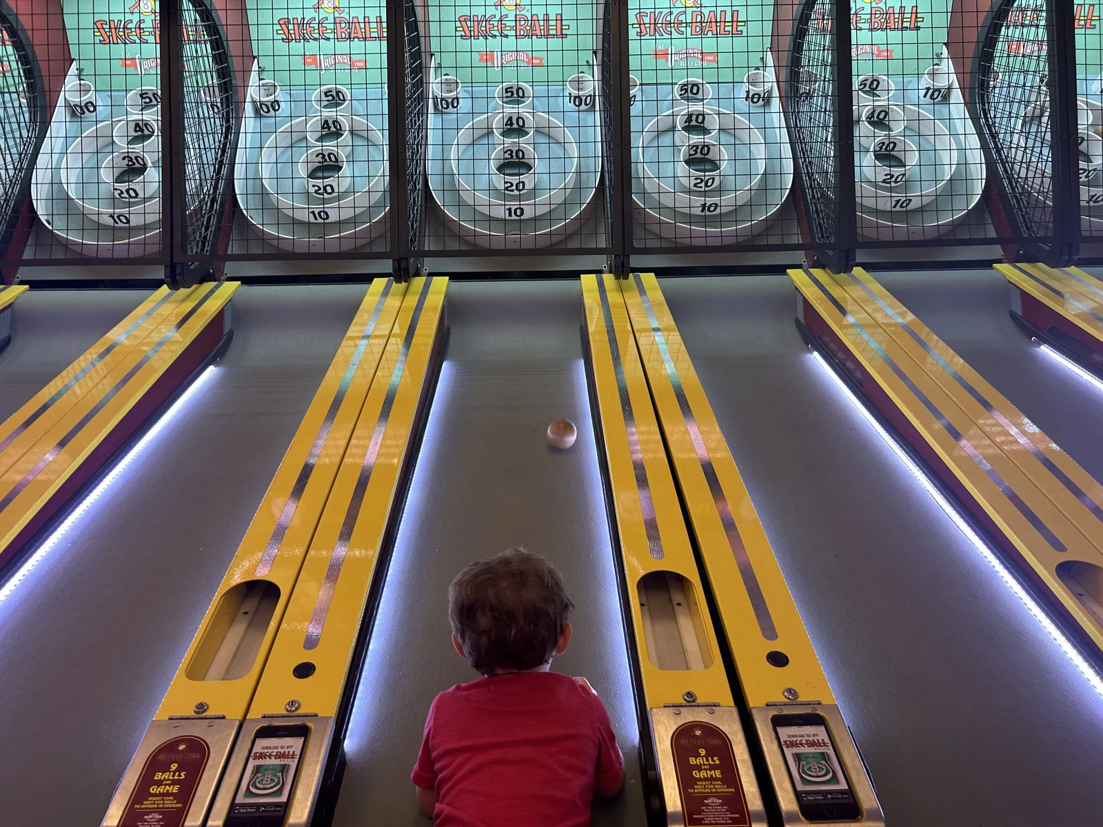 Rows of lit skee-ball lanes in the Fantasy Island arcade, seen over a young player's shoulder