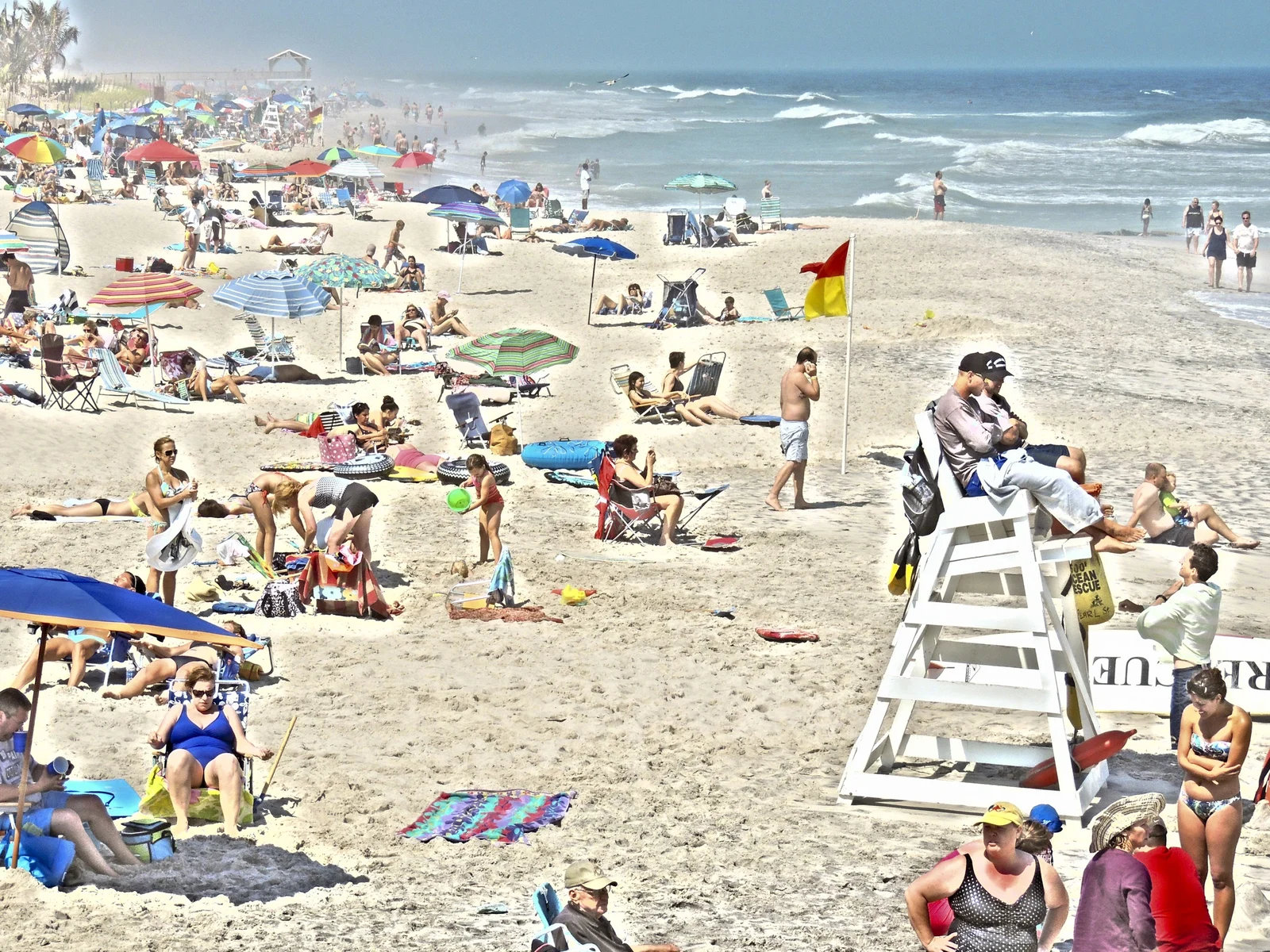 Crowded summer beach with umbrellas, a lifeguard stand and waves rolling in at Pearl Street