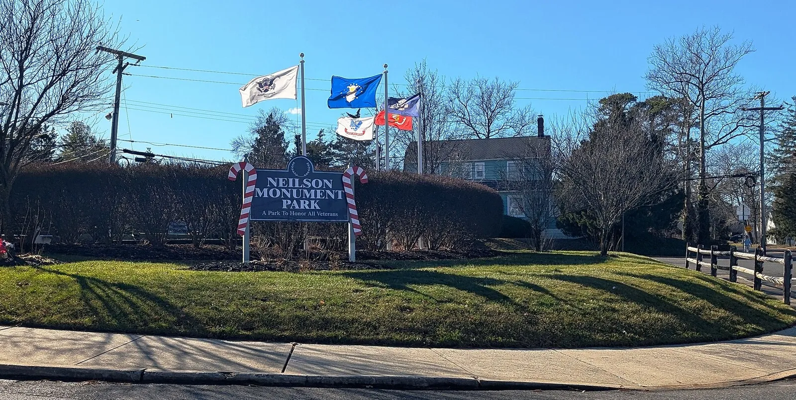 Neilson Monument Park sign with flags flying above a trimmed lawn on a sunny day