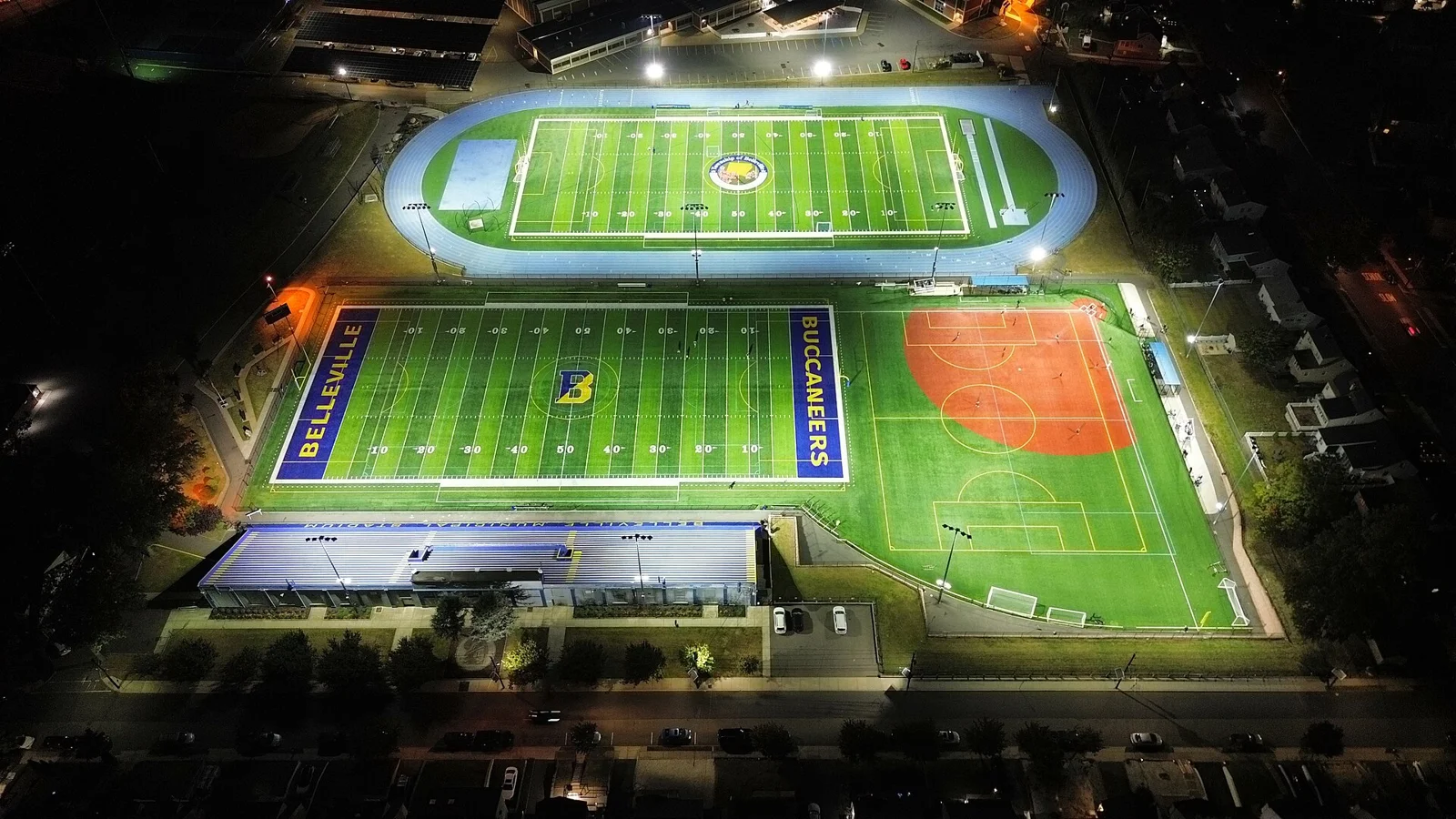 Aerial night view of the lit turf football field, track and softball field at Belleville High School