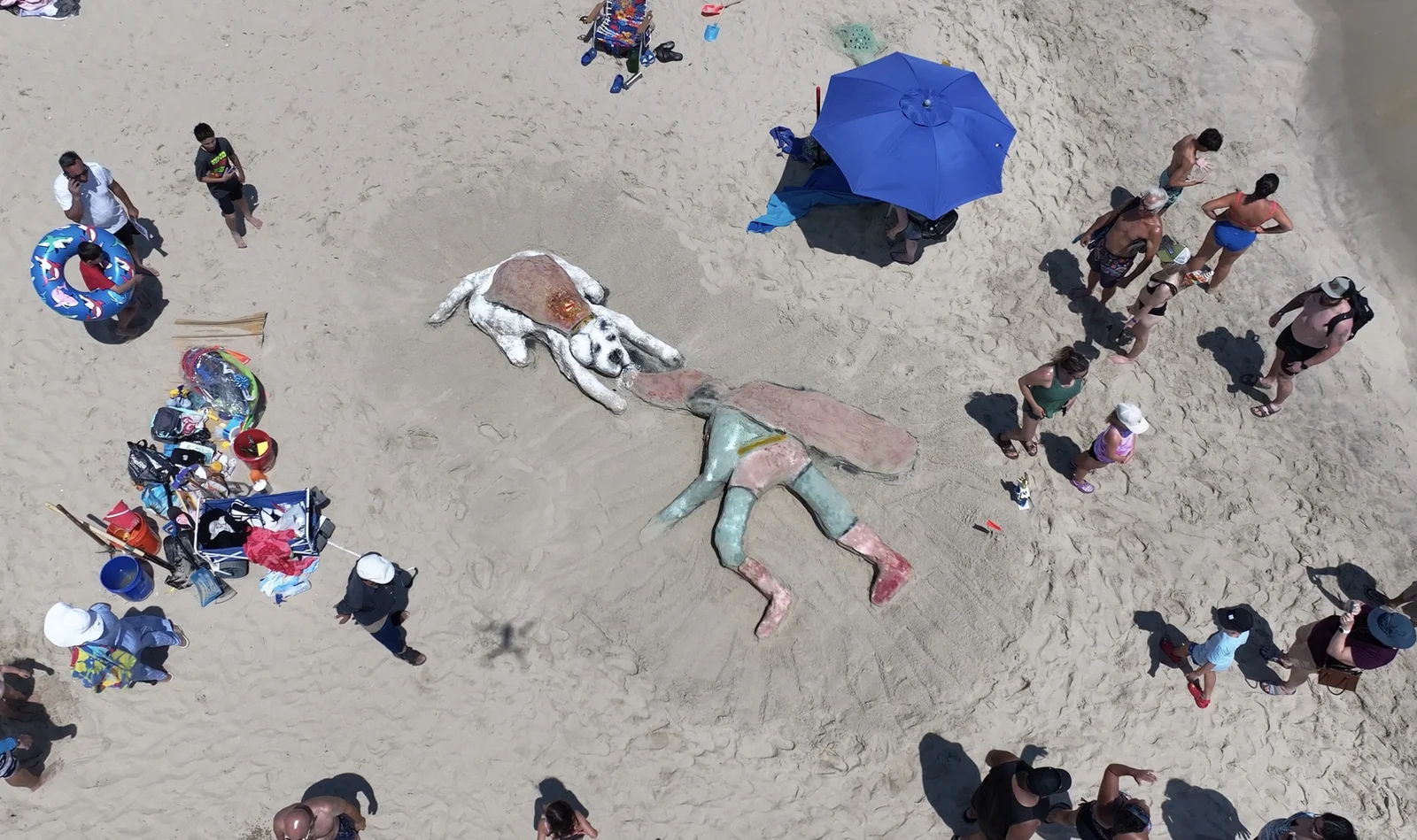 View from above of large painted sand sculptures on Belmar beach with builders, umbrellas and beach gear around them