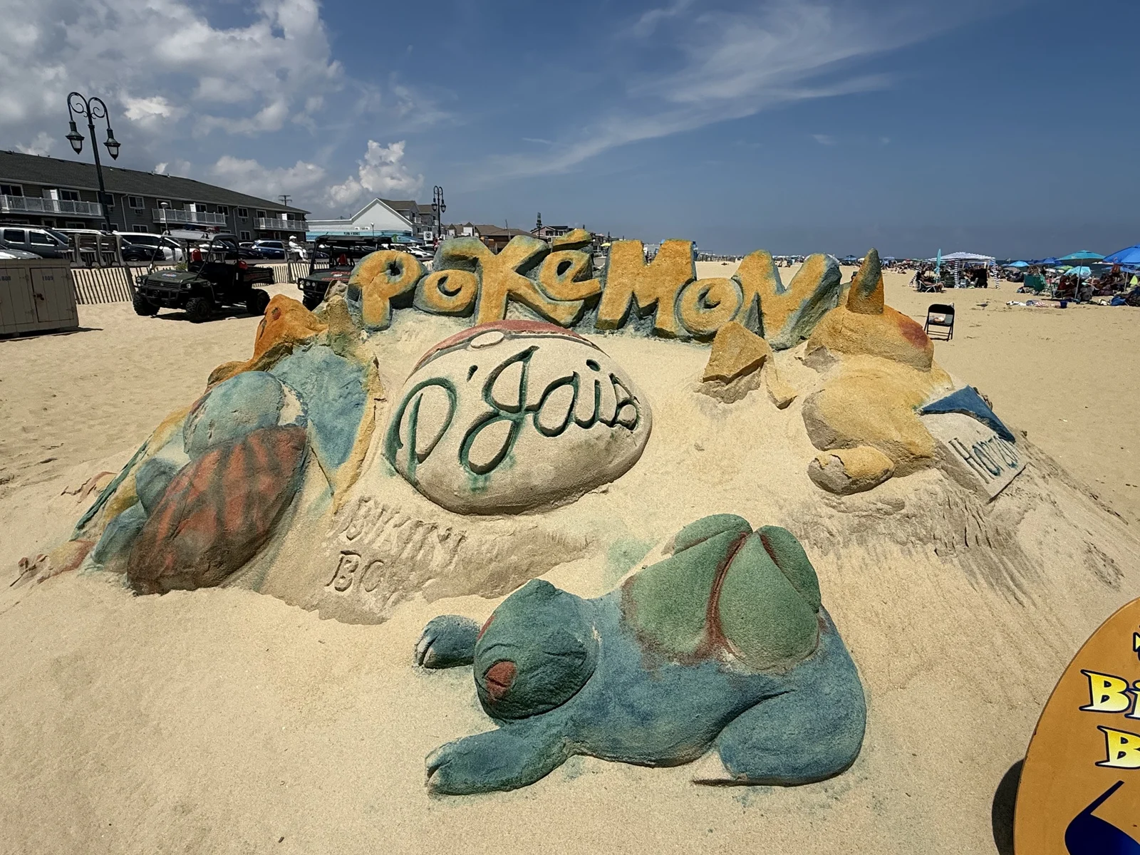 A painted sand sculpture of Pokemon characters with a carved D'Jais sign on Belmar beach, with the boardwalk and beach umbrellas behind it