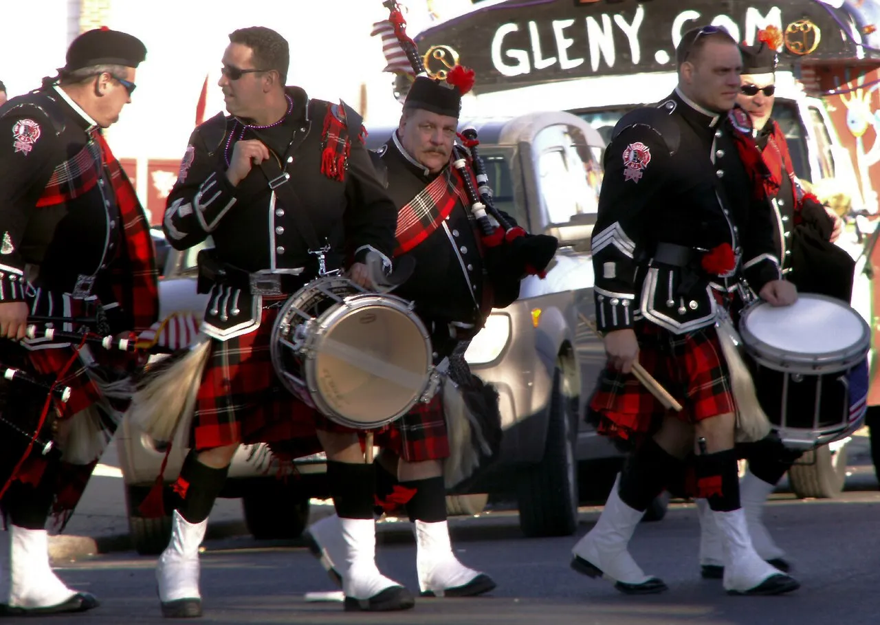 Bagpipers and drummers in kilts and black jackets marching down the street in a parade