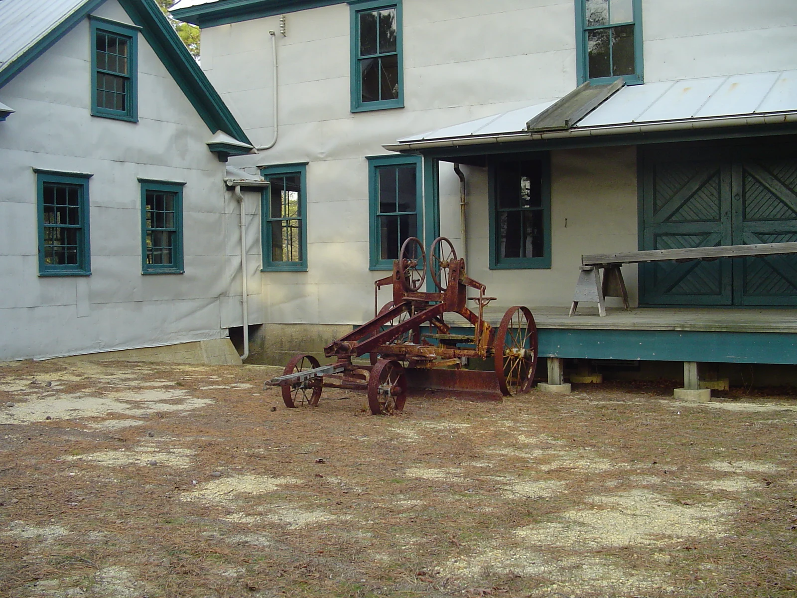 A white cranberry processing building with green trim and antique farm machinery in the yard at Double Trouble