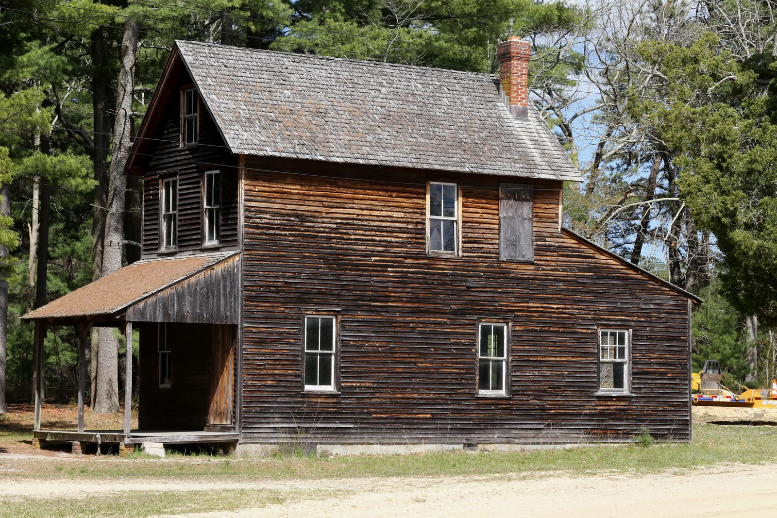A weathered two-story wooden house with a side porch among pine trees in the Double Trouble historic village