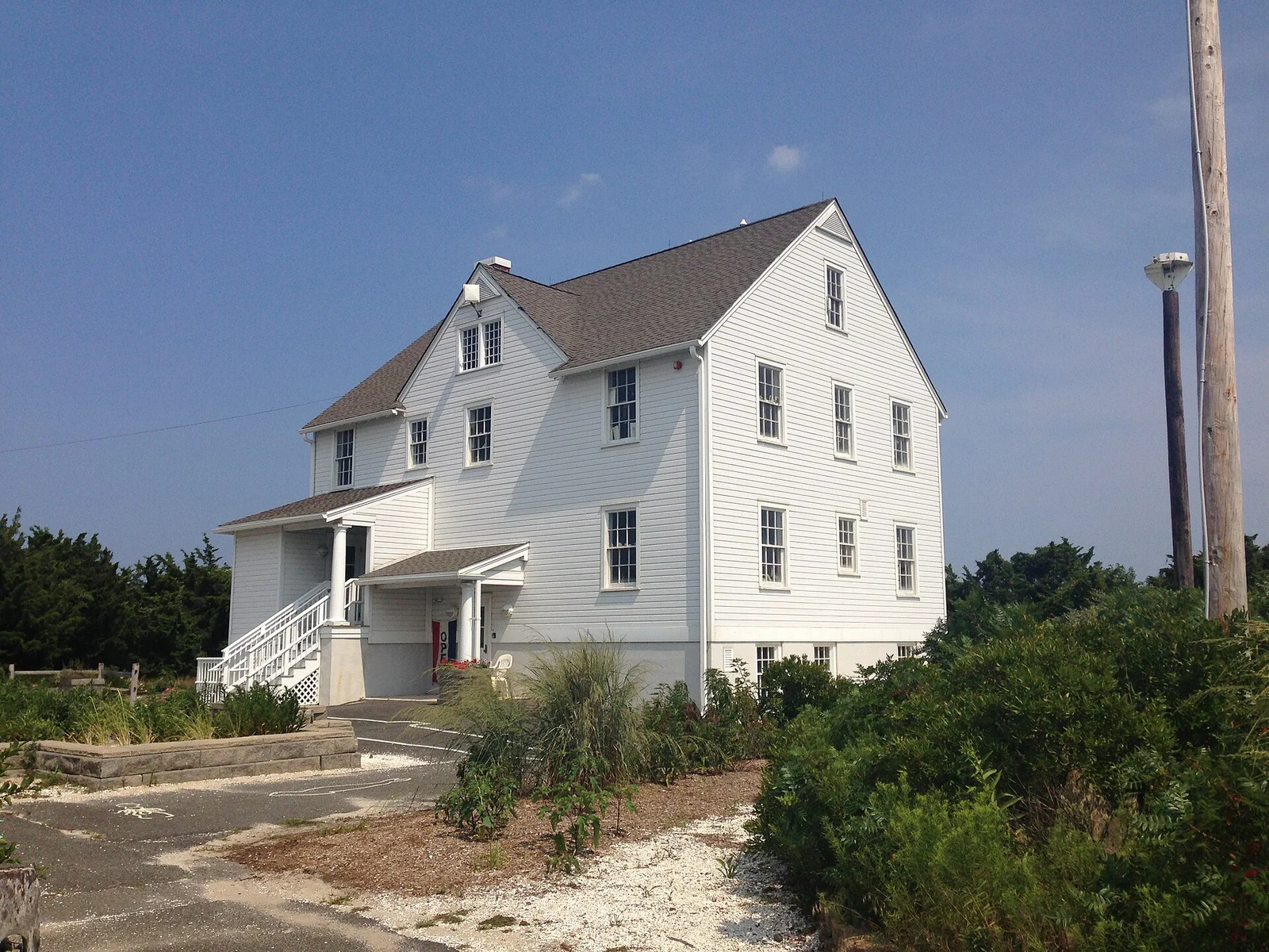 A tall white clapboard building with a gabled roof among dune shrubs at Island Beach State Park