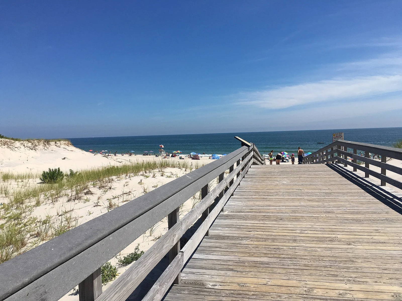A wooden boardwalk crossing the dunes to the ocean beach at Island Beach State Park on a sunny day