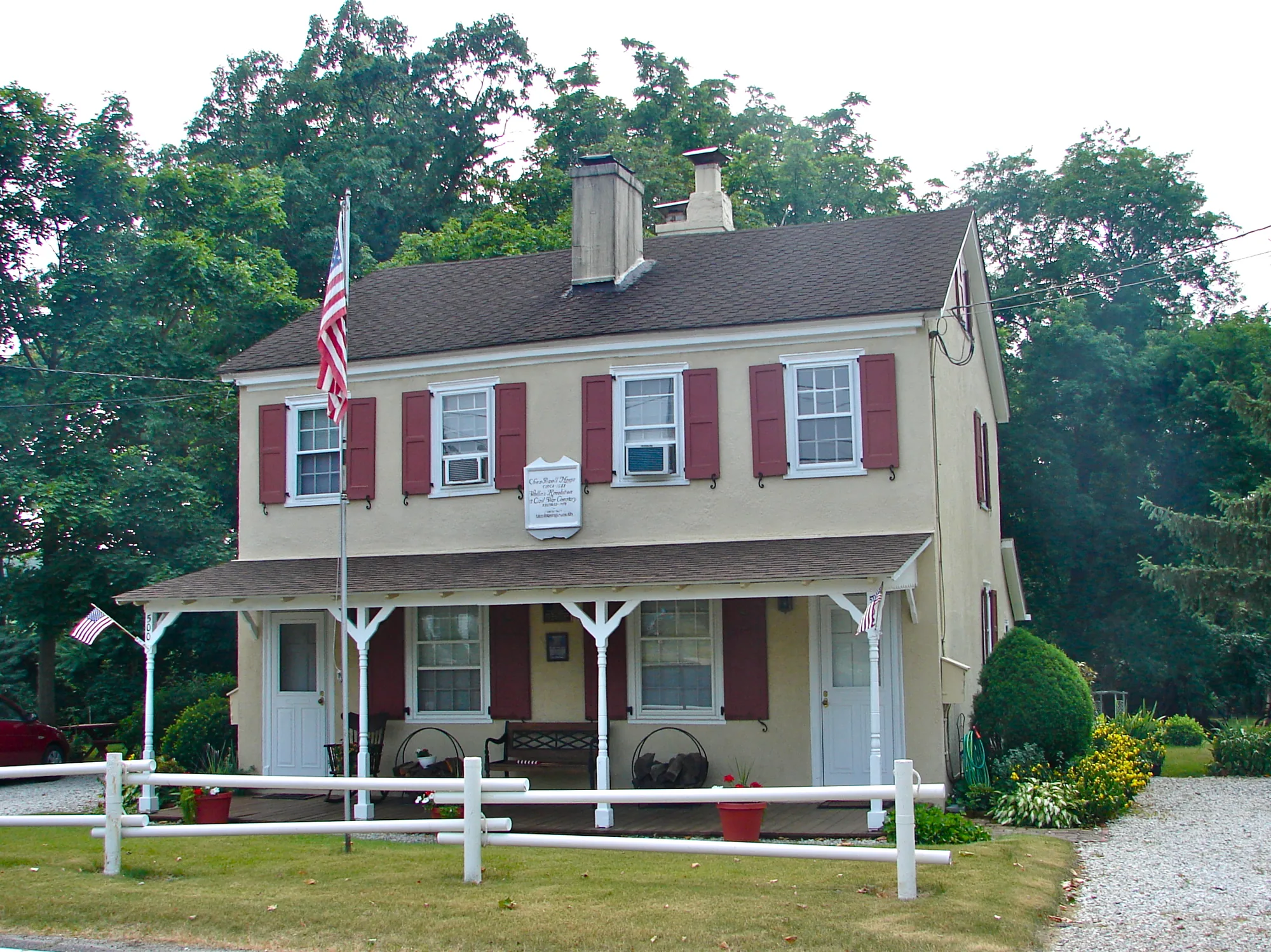 A white two-story colonial farmhouse with a side wing, set back on a wide lawn