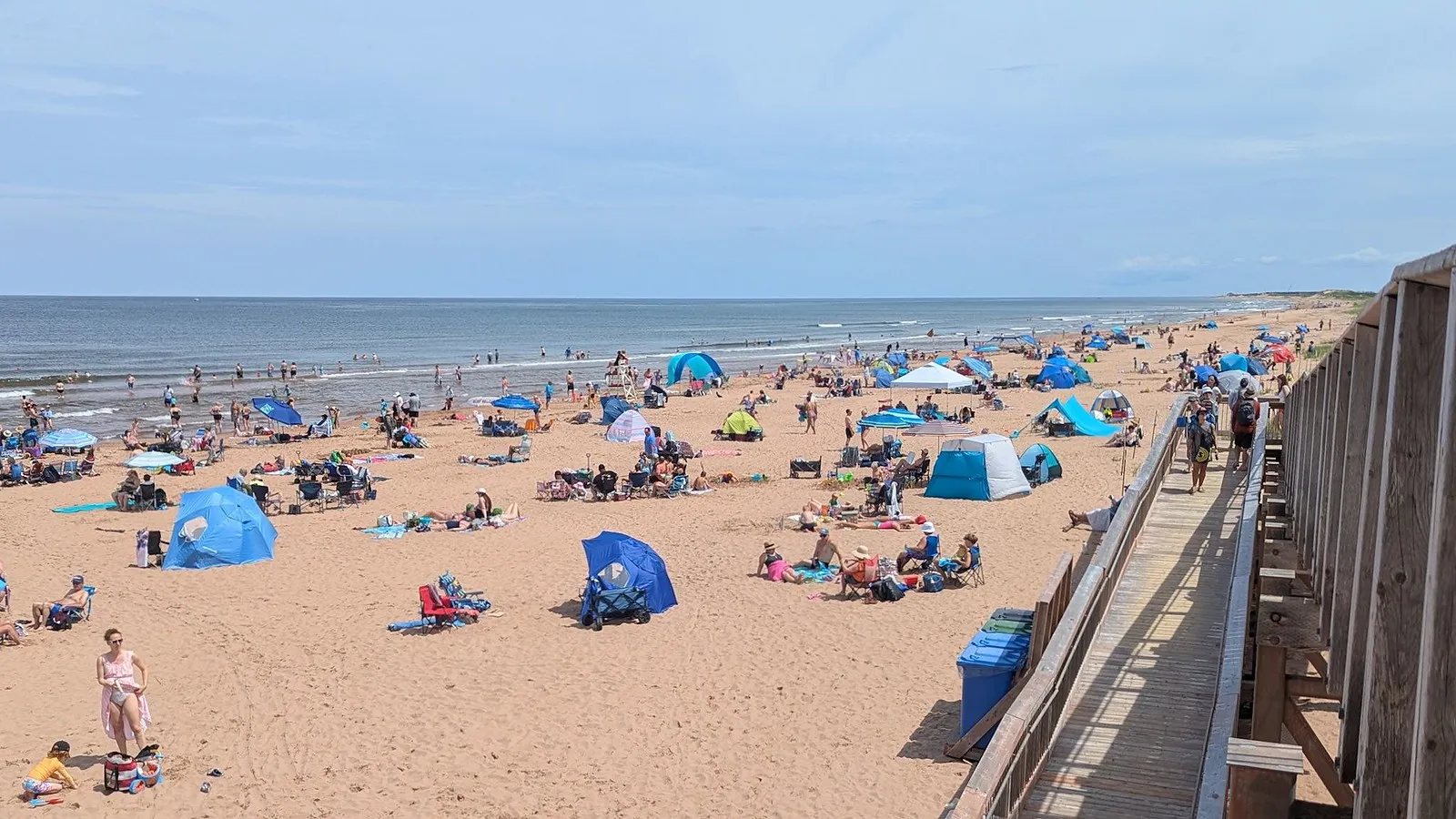 A busy summer beach at Bradley Beach with umbrellas and tents beside the boardwalk rail