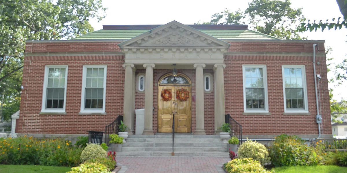 The brick Bradley Beach Public Library with white columns framing its front doors and flower beds by the steps