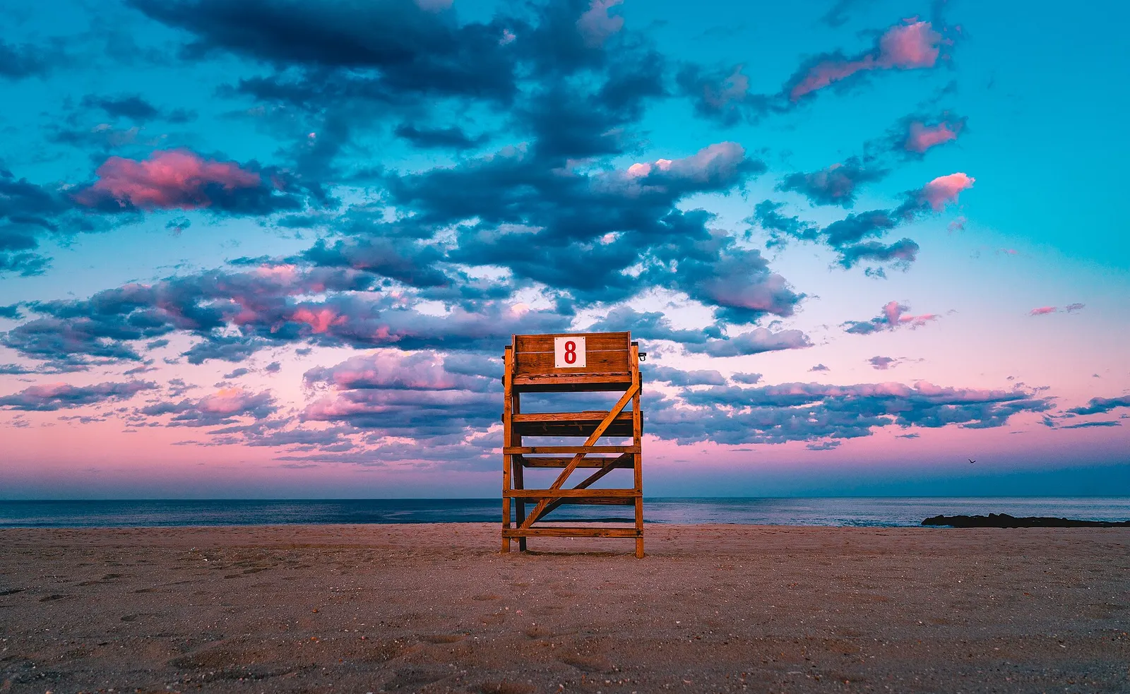 A wooden lifeguard stand on the Bradley Beach sand under a vivid blue and pink sky
