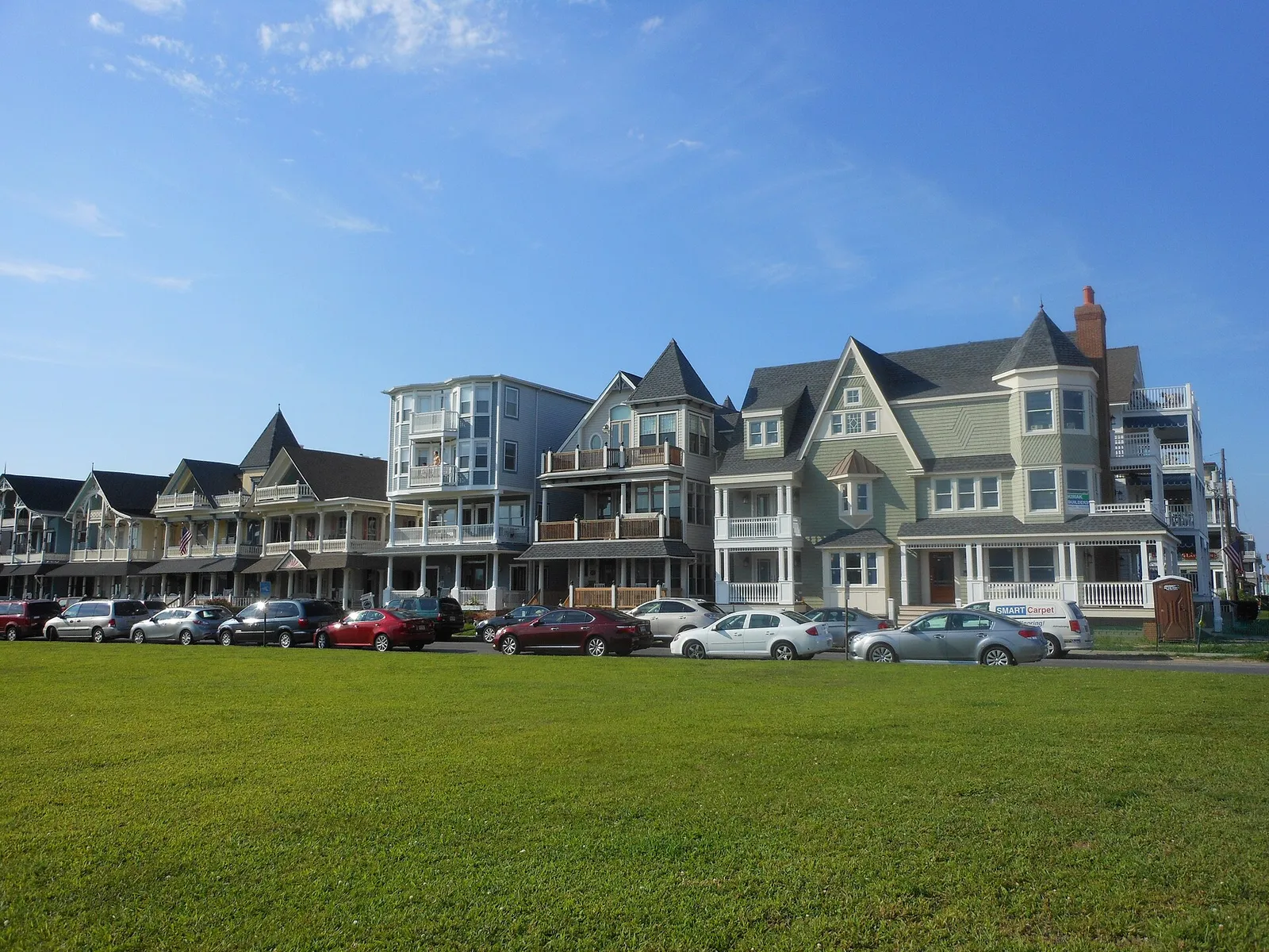 A row of Victorian homes with turrets and porches along Ocean Avenue in Bradley Beach, seen across a green lawn