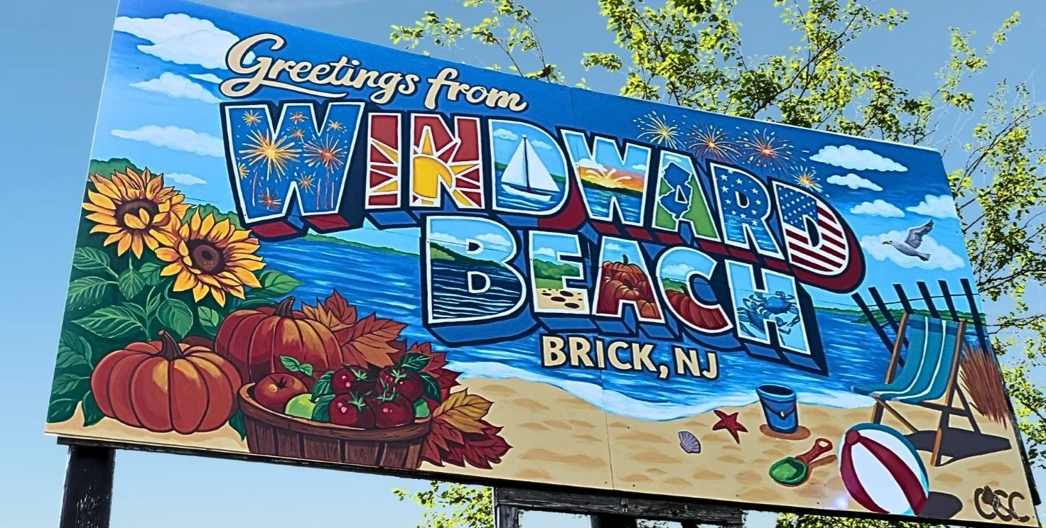 Colorful postcard-style sign reading Greetings from Windward Beach, Brick, NJ, with sunflowers and a beach chair