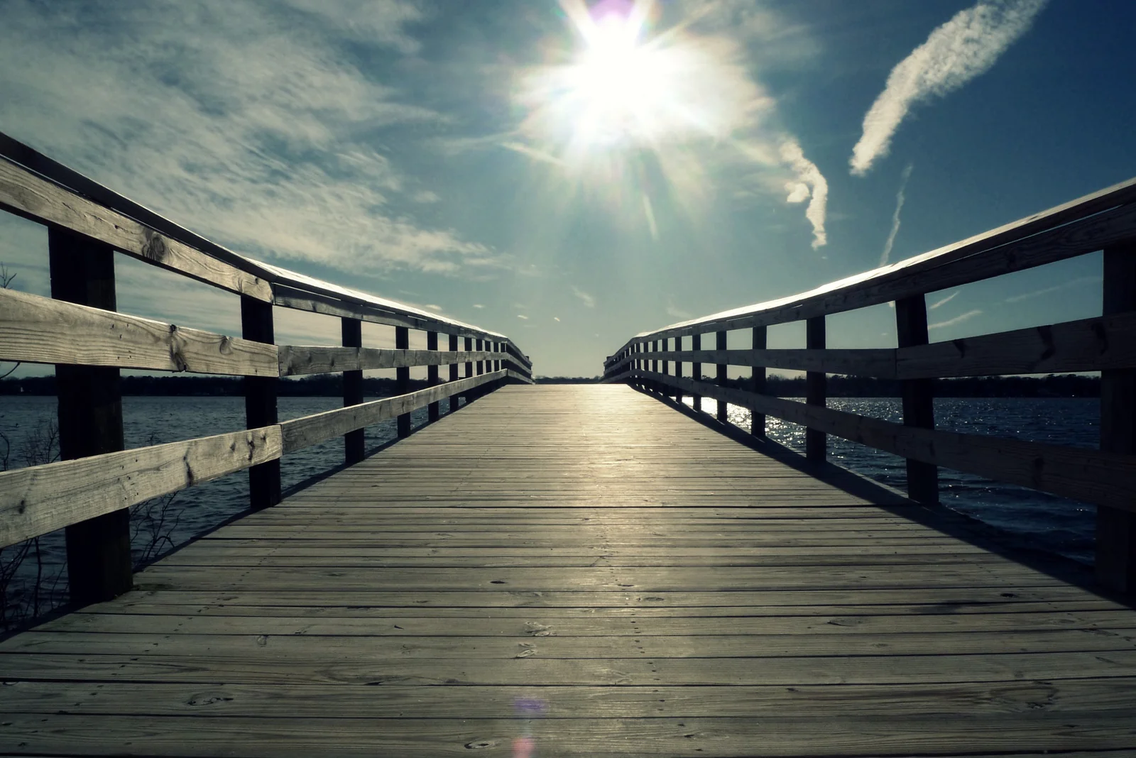 Wooden fishing pier stretching over the Metedeconk River at Windward Beach Park, sun overhead