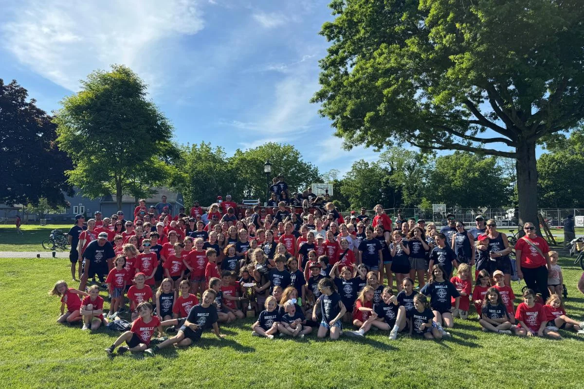 A large crowd in red and navy team shirts gathered on the lawn under shade trees for the North vs. South Challenge